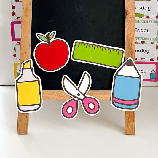 Blackboard with educational cutout items including an apple, ruler, bottle, scissors, and pencil.