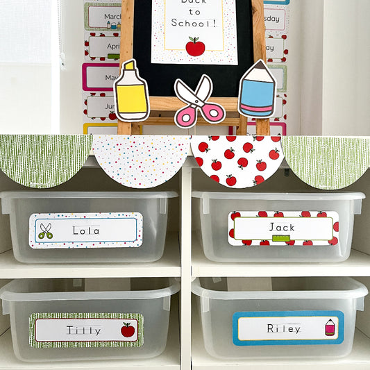 Storage bins with personalised labels on a shelf, with classroom-themed decorations in the background.