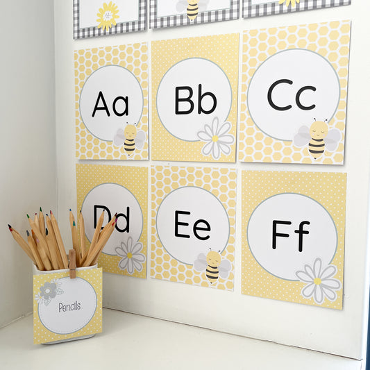 Alphabet flashcards with letters A to F, a container of pencils, and decorative bee themed elements on a white surface.