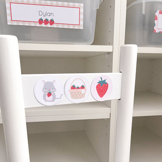 White children's chair in front of shelf with colourful labels featuring a strawberry, basket, and mouse design.
