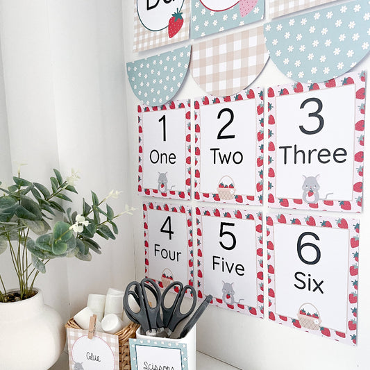 Children's educational cards with numbers and letters on a white wall in a strawberry theme.