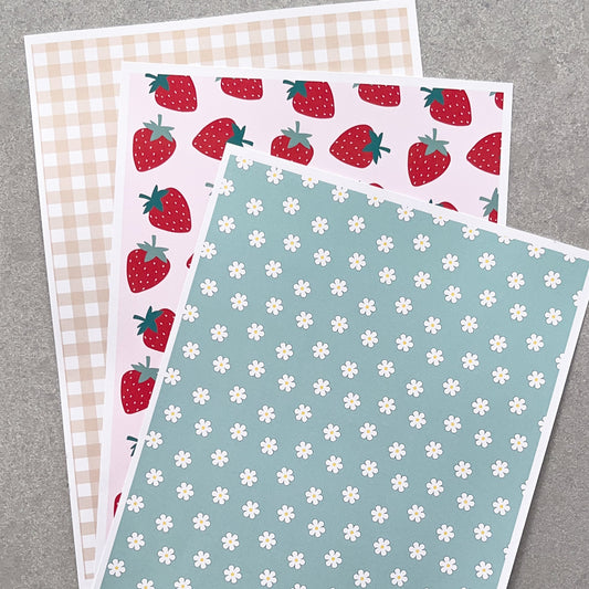 Three sheets of patterned paper with different designs on a grey background