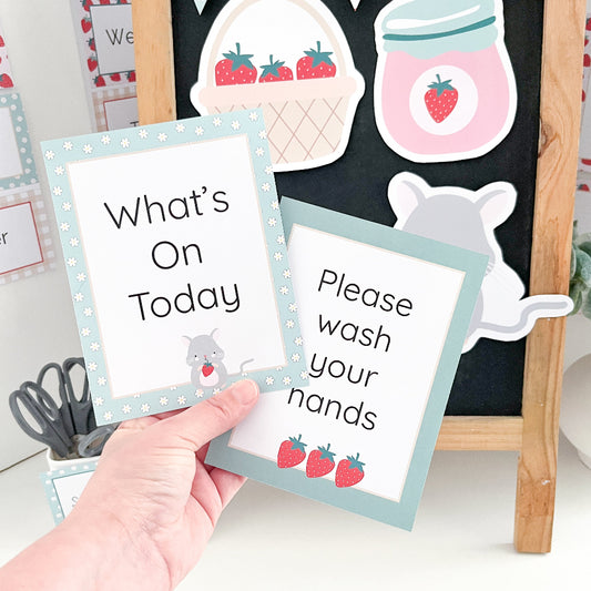 Hand holding a card with 'What's On Today' and 'Please wash your hands' text, with educational posters in the background.