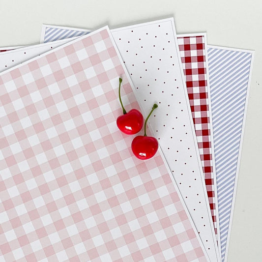 Cherry themed patterned papers spread out on white background.
