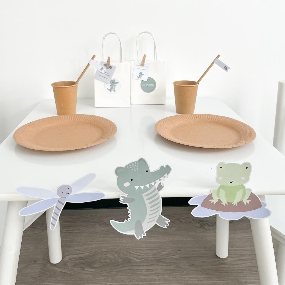Crocodile, Frog and Dragonfly bulletin board accents stuck on white party table. There are cups plates and party bags in the background.