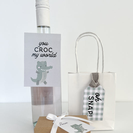 Gift bag with crocodile design and text, placed on a white surface.