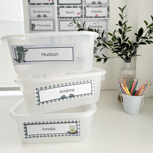 Name plate labels for classroom in a crocodile theme stacked on white bench. Classroom elements are in the background.