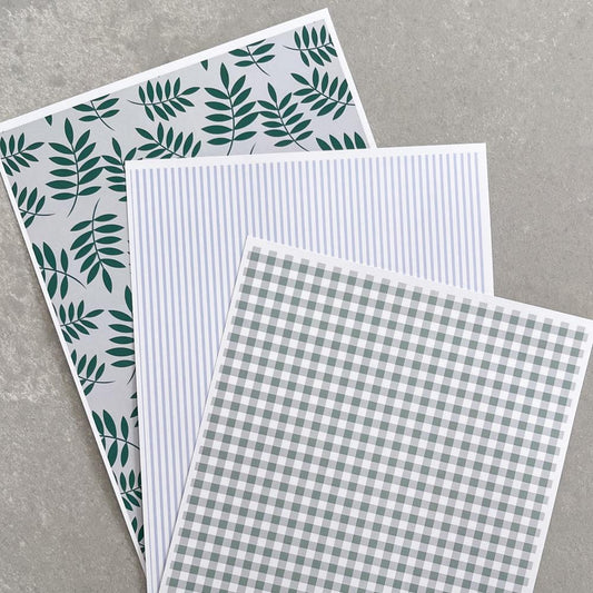 Coordinating patterned papers in blue and green displayed on grey bench.