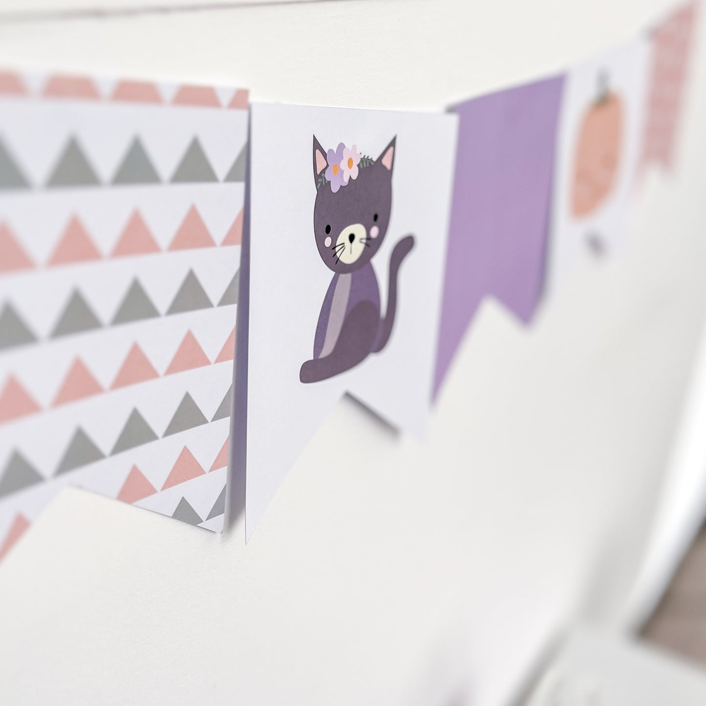 Pastel Halloween bunting with cute cate and geometric shapes hanging on white wall.