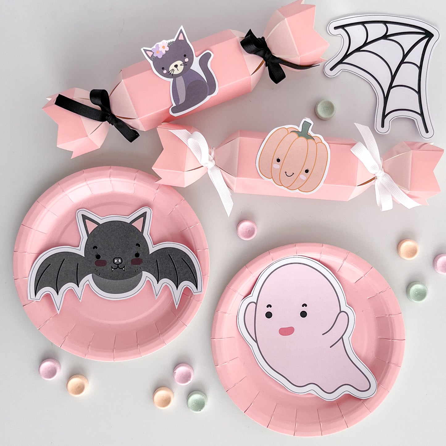 Pastel halloween graphics on pink party plates and treat crackers spread out on white table.