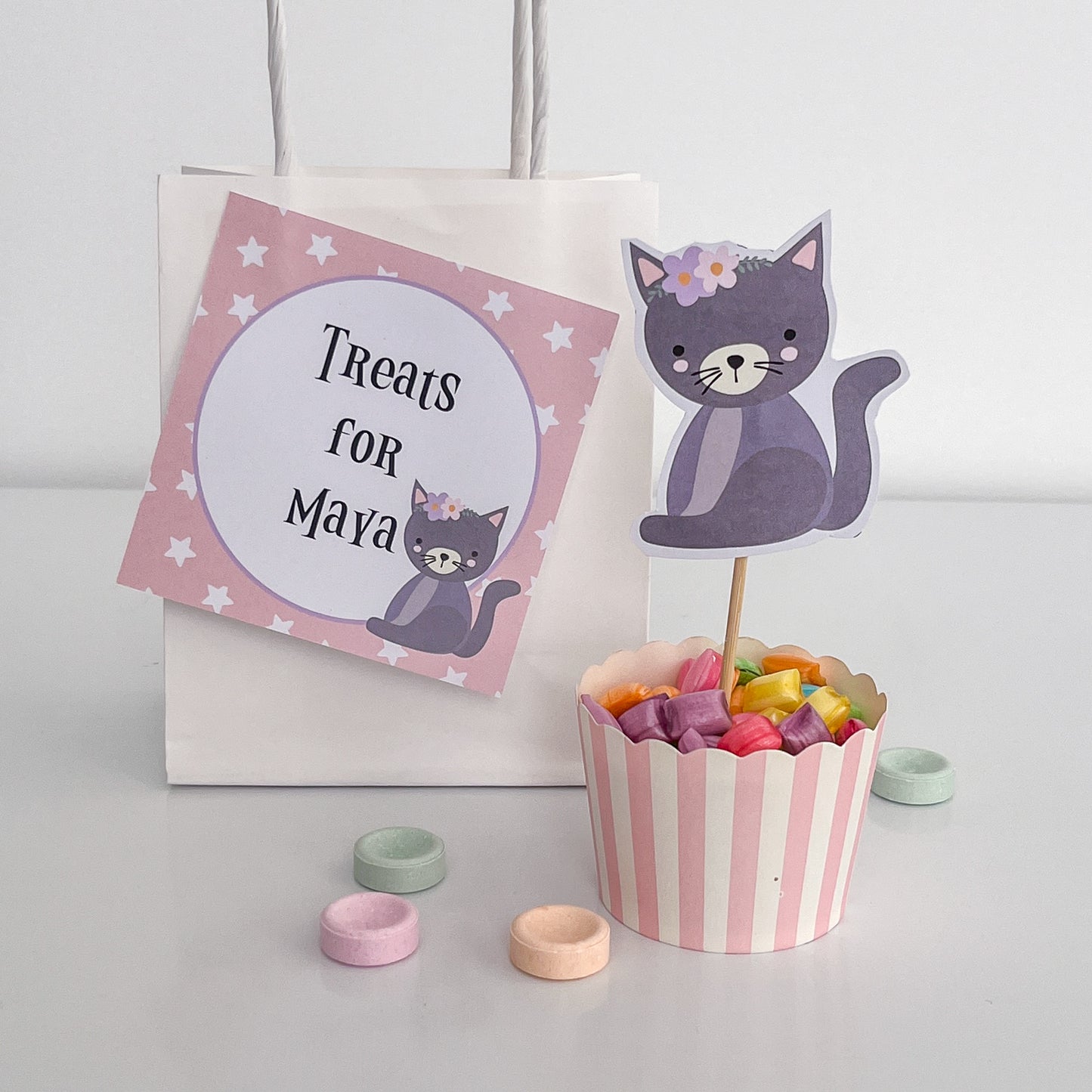 Cute pastel halloween cat and treat bag printables displayed with candy on a white table.