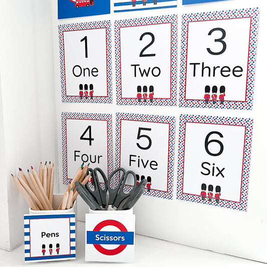Educational number posters with corresponding words and illustrations, placed on a white surface with stationery items.
