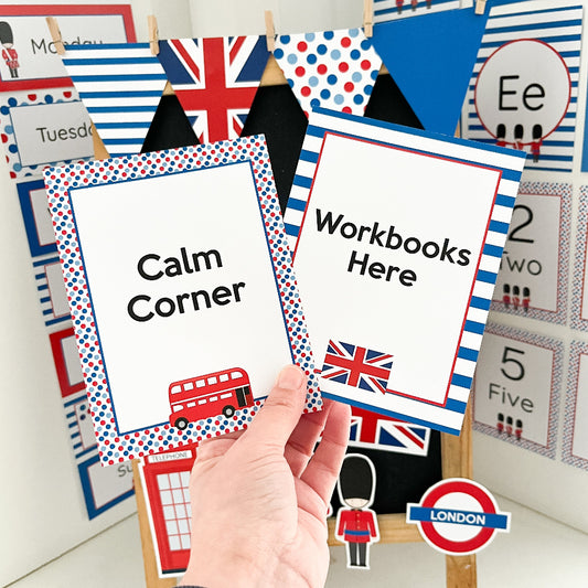 Classroom signs with British-themed graphics, including a hand holding a 'Calm Corner' sign in front of educational posters on a white wall.