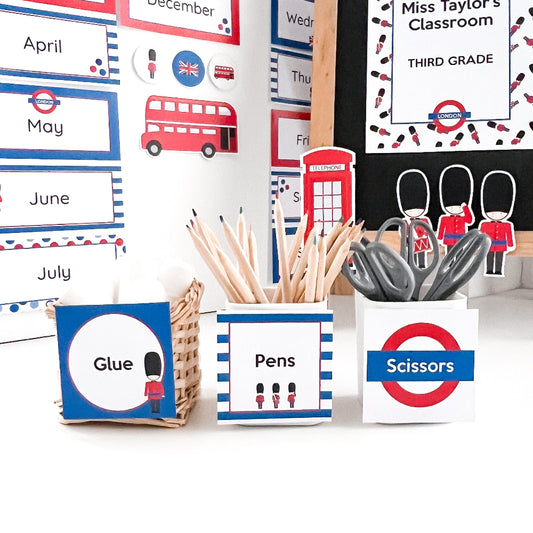 Classroom supply bins with labels for glue, pens, and scissors against a wall with educational posters.