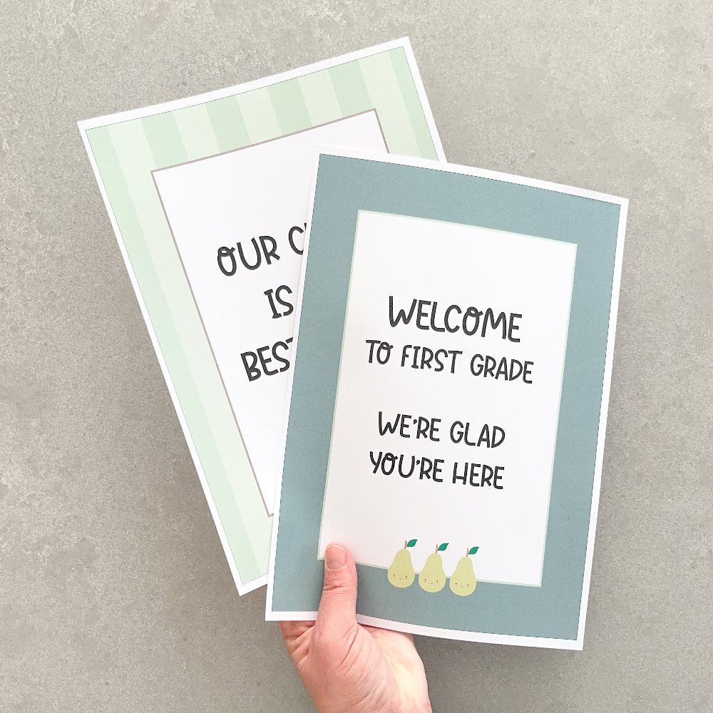 Two classroom signs on a grey surface, one held by a hand.