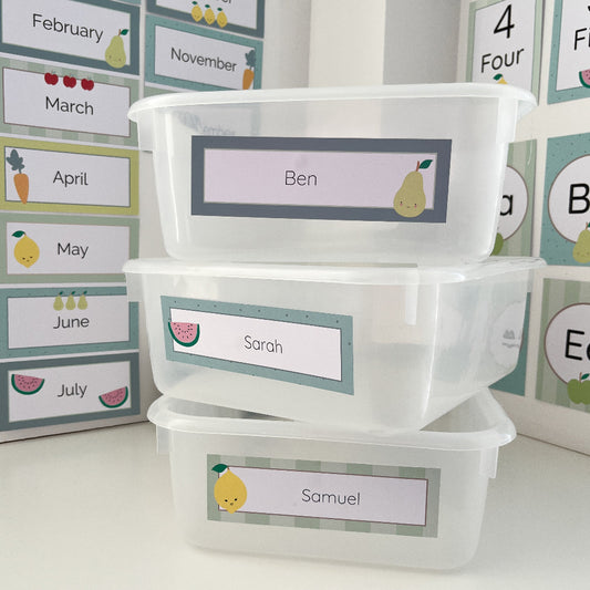 Stack of clear containers with name labels on a white surface with educational posters in the background.