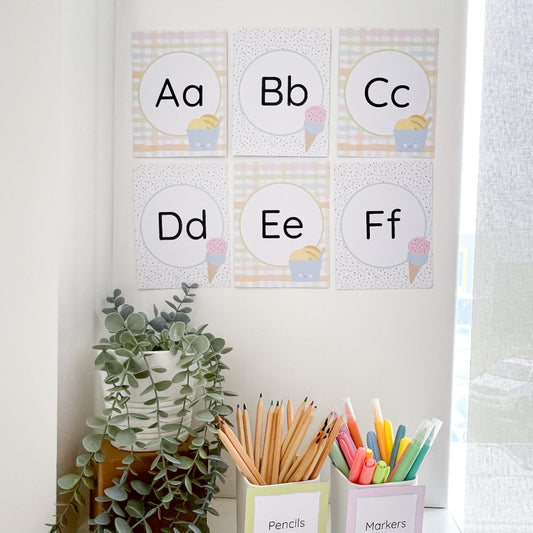 Alphabet flashcards with ice cream illustrations on a white wall, below which are containers of pencils and markers.