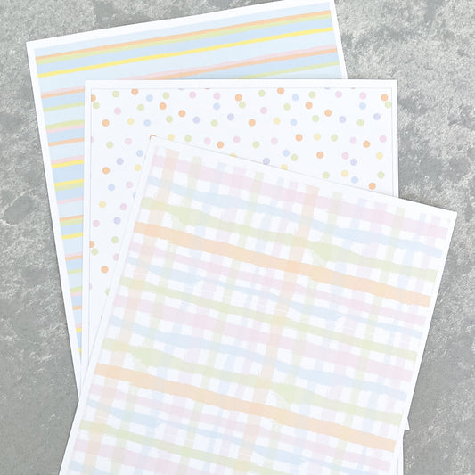 Three sheets of paper with different pastel patterns on a gray surface