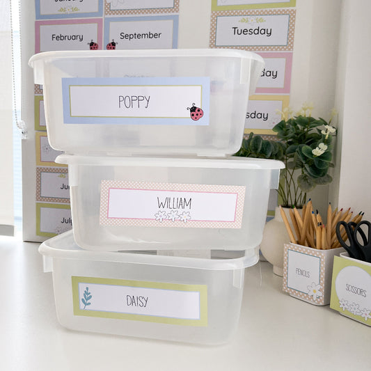 Stack of labeled storage bins with names 'Poppy', 'William', and 'Daisy' on a desk.