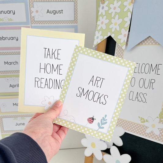 Hand holding a card with 'Art Smocks' text, surrounded by other educational posters.