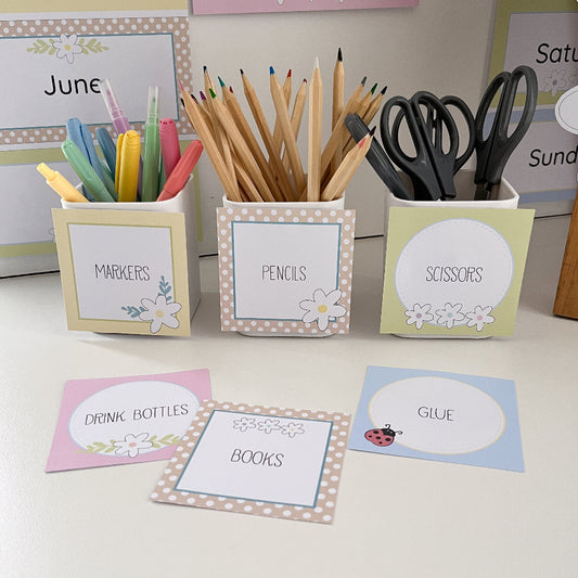 Stationery items including markers, pencils, scissors, and glue with labeled containers on a table.