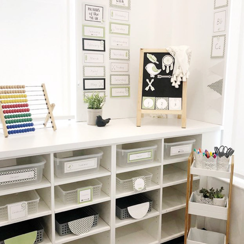A classroom setting featuring green, white and black classroom decor, surrounded by shelves with educational decor and supplies.