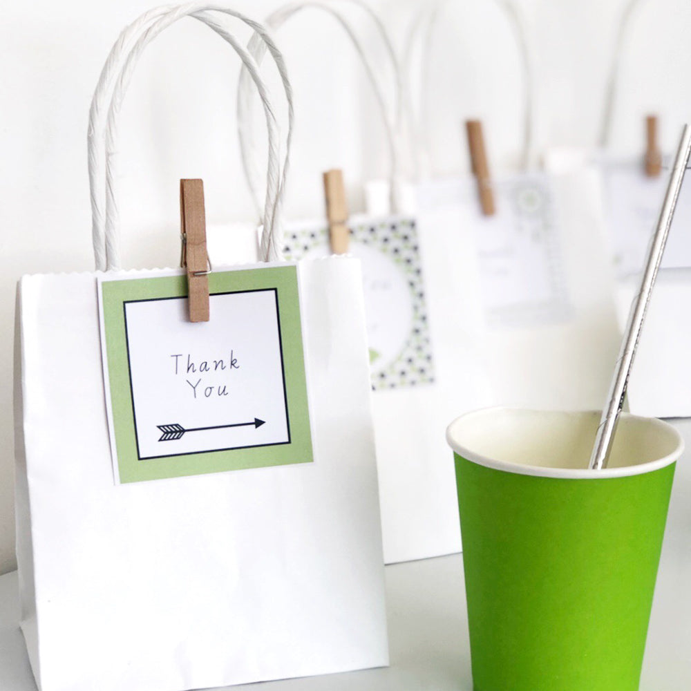 Green and black editable square labels on a party table set up on white background. There is a green cup in the foreground.