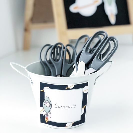 Square classroom labels with a rocket and planets placed onto a white caddy of scissors