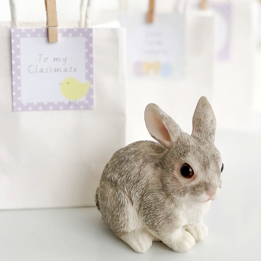 Cute bunny statue in front of Easter treat bags on white table.