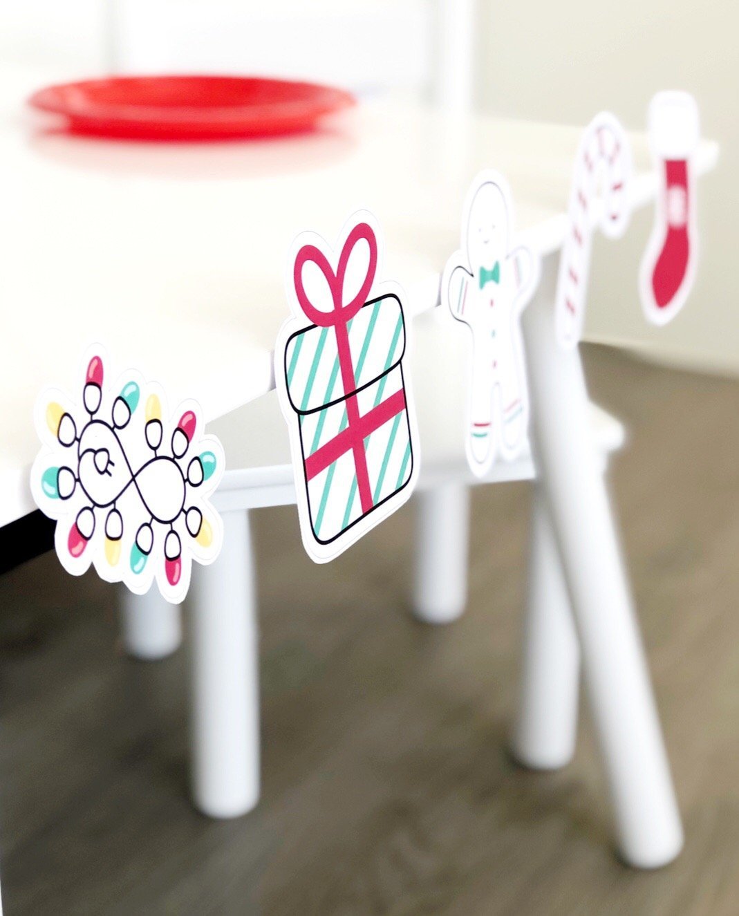 Christmas theme printable cut outs in bright red and green stuck to a white table.