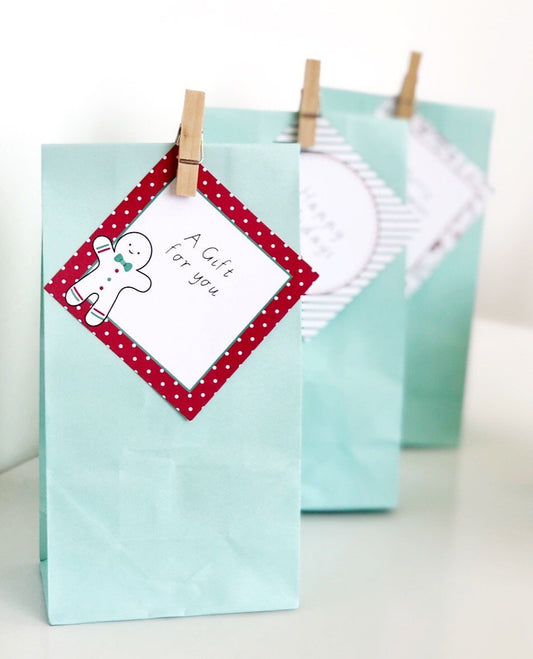 Editable square gift tags in red and green Christmas theme pegged onto green treat bags.