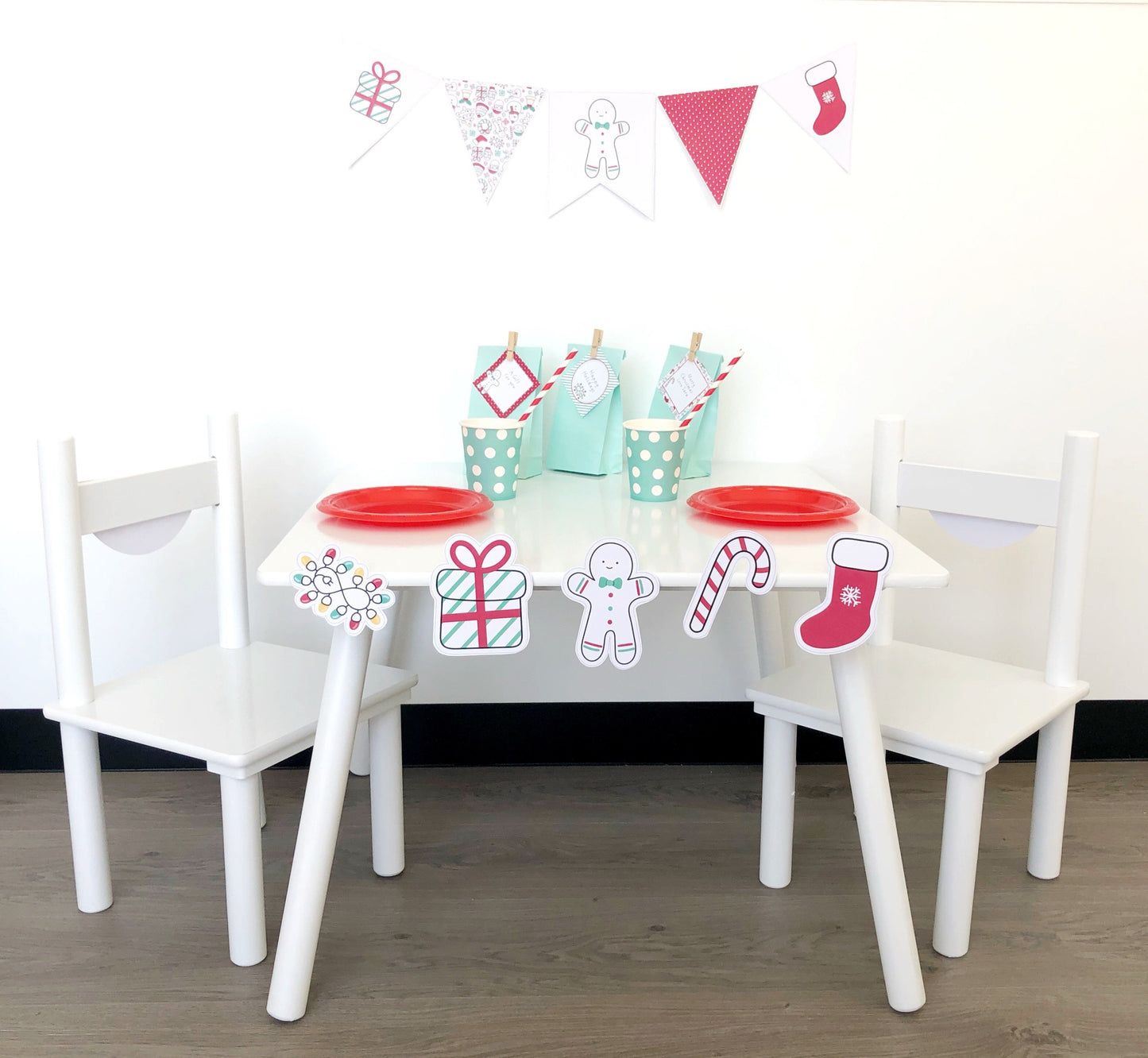 A set of three white chairs with a Christmas-themed decoration pack, including bunting, flags, and gingerbread man cutouts, with a table in the middle.