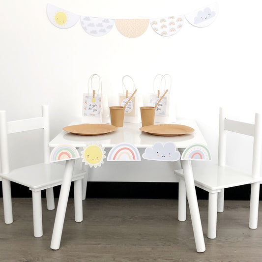 Pastel rainbow theme party set up with white table and chairs and scalloped bunting on the wall.