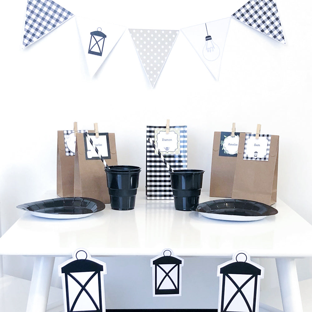 Black and White farmhouse theme party table with party bags, bunting flag, plates and cups. Lantern shapes are placed on the white table.