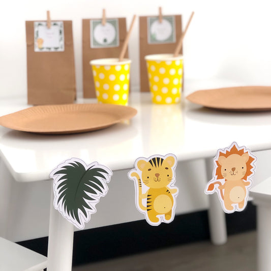 A set of mini party decorations featuring safari animals such as a giraffe, lion, and monkey, with a yellow polka-dotted background, displayed on a table.