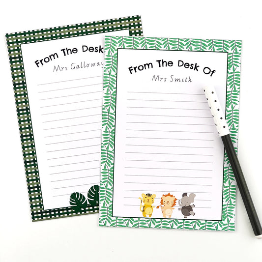 Safari themed editable note paper with cute safari animals and jungle leaves. Displayed next to a black pen on a white desk.