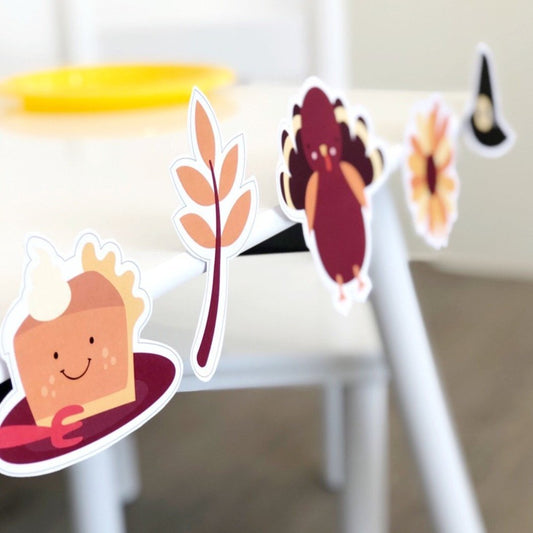 A set of colorful mini party decoration pack printable files featuring various Thanksgiving-themed designs, such as a pumpkin, a turkey, and leaves, displayed on a table.