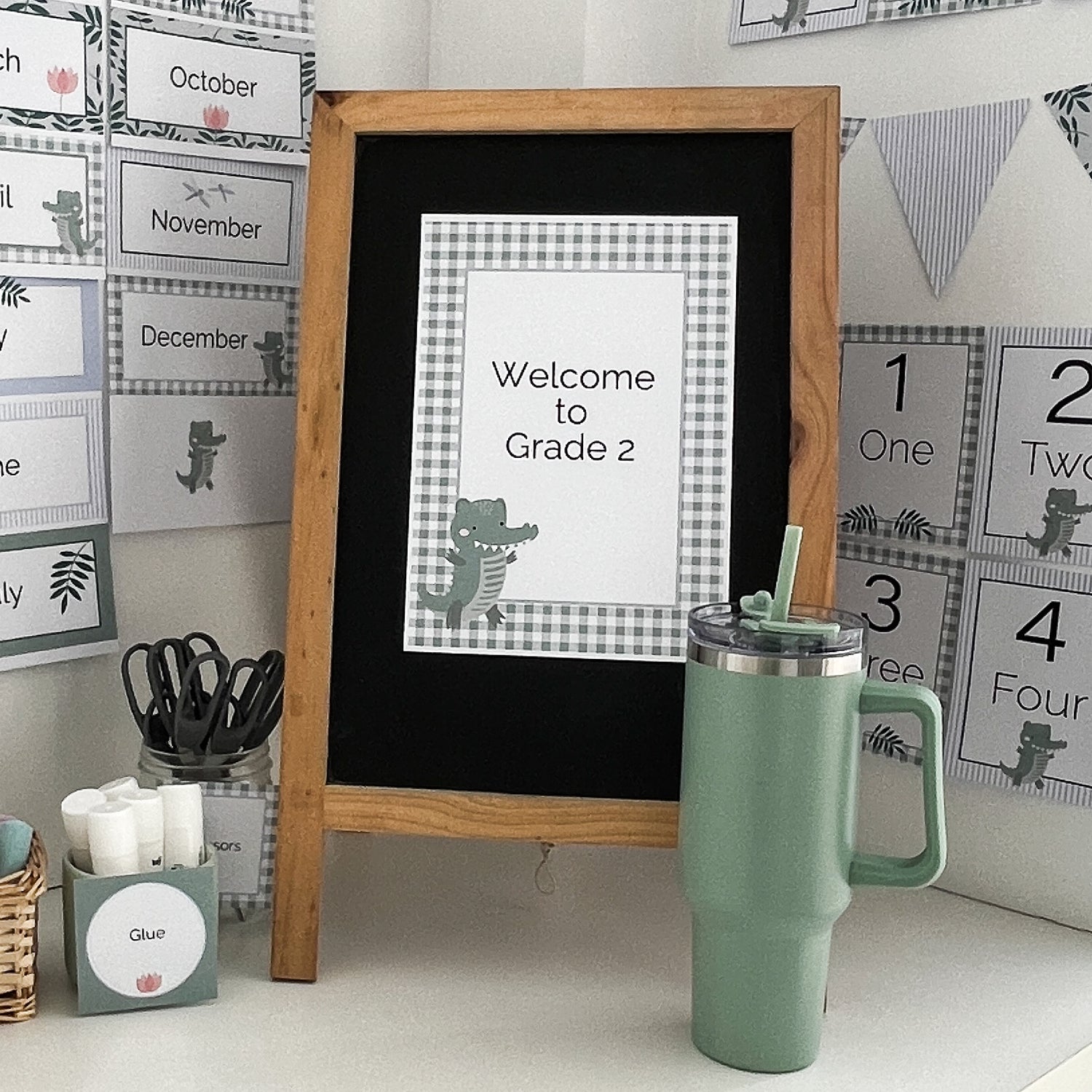 Classroom welcome sign in a crocodile theme. Sign is stuck to blackboard and is pictured with a drink bottle and calssroom supplies