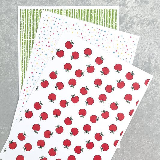 Sheets of paper with red apples and bright patterns on a grey surface