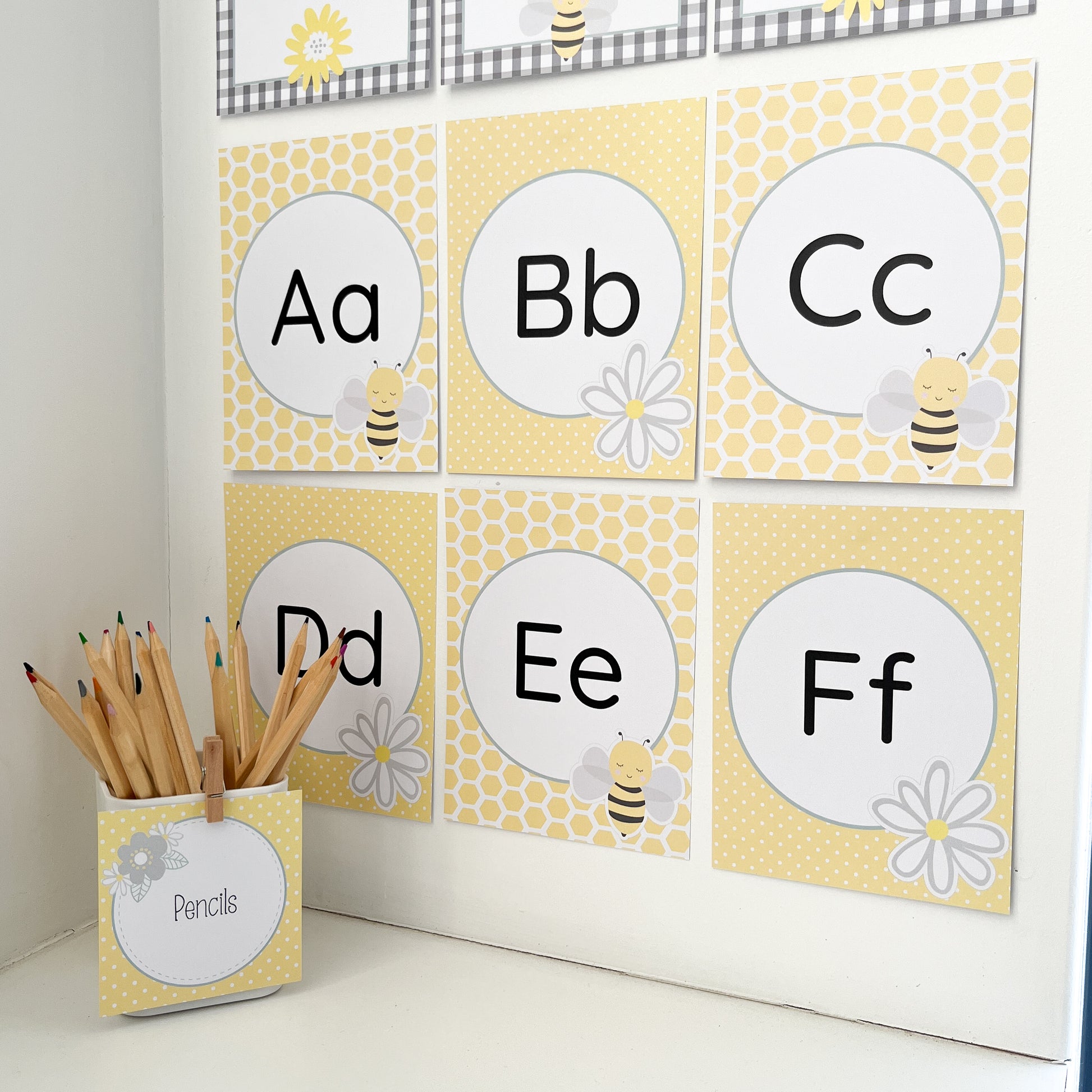 Alphabet flashcards with letters A to F, a container of pencils, and decorative bee themed elements on a white surface.