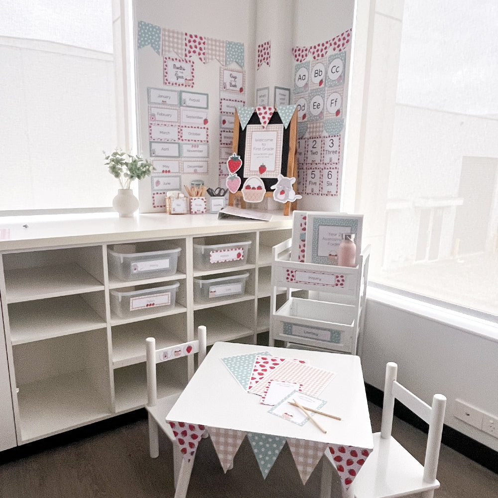 Classroom with white table and chairs, storage shelves, and educational strawberry themed posters on the wall.