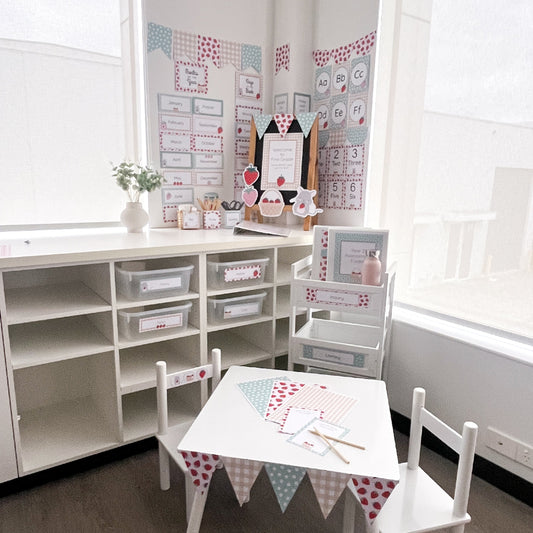 Classroom with white table and chairs, storage shelves, and educational strawberry themed posters on the wall.