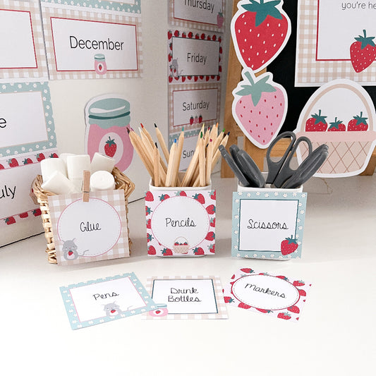 Stationery items with strawberry-themed labels on a white surface in a classroom.