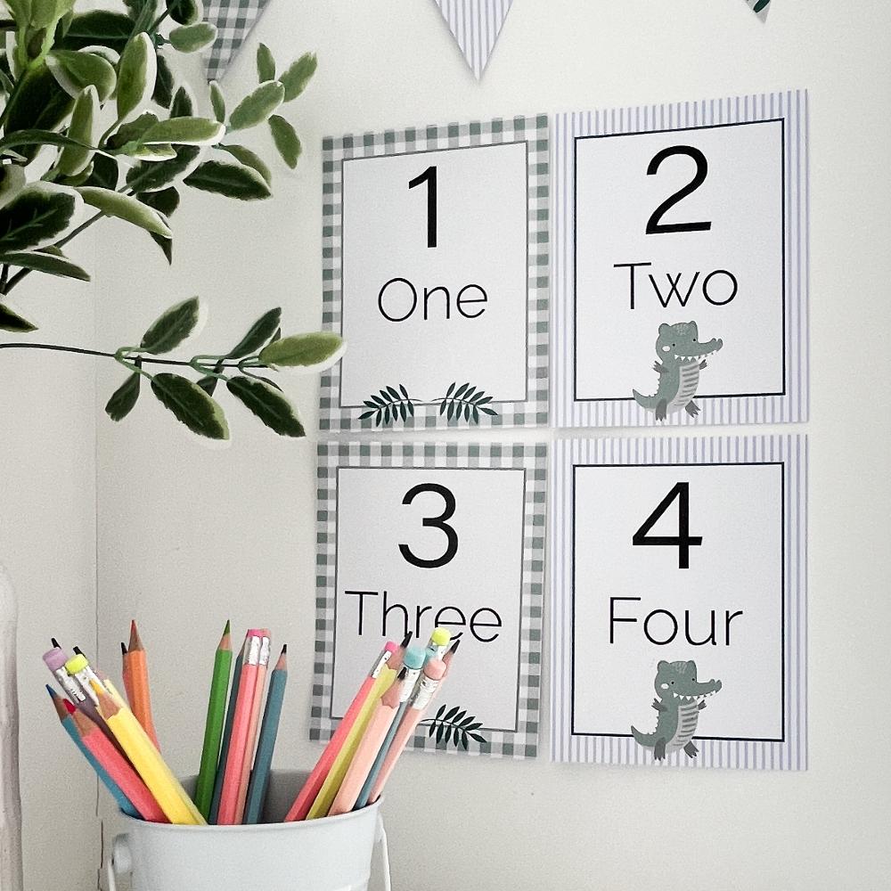 Crocodile theme educational number flash cards on white wall in classroom with pencils, bunting flag and plant on desk.