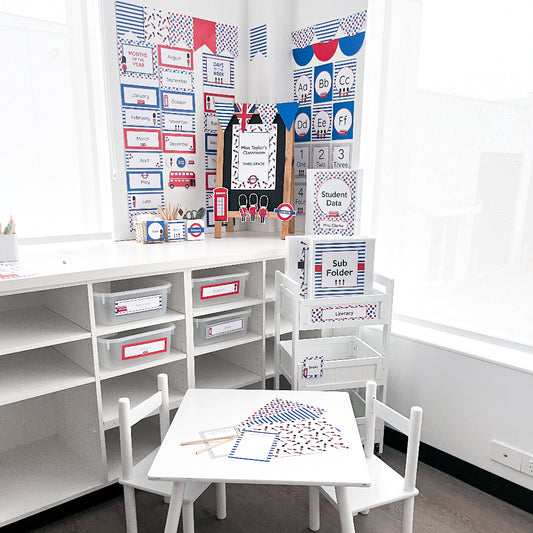 Children's classroom setup with white furniture, colourful educational posters, and a small table all in a red, white and blue British theme. 
