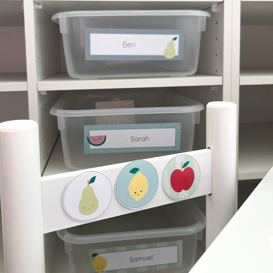 White children's chair is decorated with circles featuring fruit and is front of classroom locker tubs. 