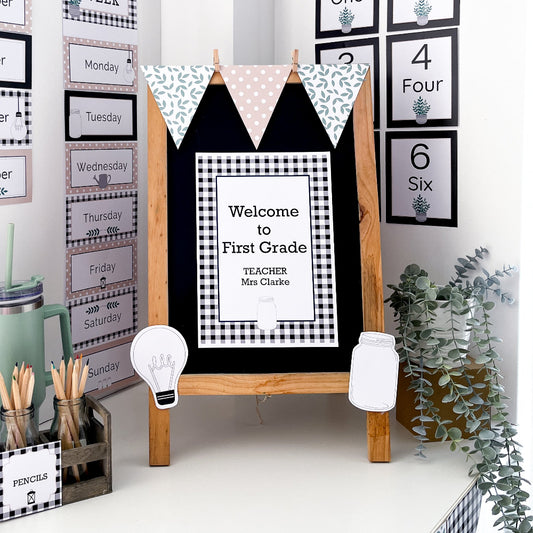 Classroom Balckboard easel decorated with bunting flags, sign and bulletin board cut outs on a white shelf. The farmhouse themed decorated classroom is in the backgorund. 