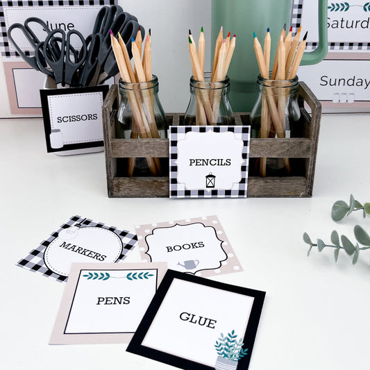 Classroom printable labels laid out on white bench. In the background the labels are on school supplies like pencils and scissors. 