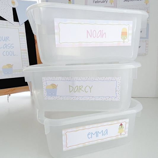 Clear plastic storage bins with personalised labels on a white surface.