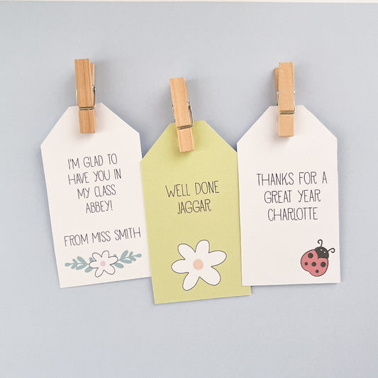 Three white tags with printed messages and designs, attached to a pale blue background.
